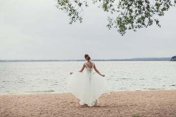 Fototapeta na wymiar Bride standing near lake coast wearing beautiful wedding dress