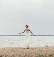 Fototapeta na wymiar happy bride in a wedding dress stands on the sand near the sea