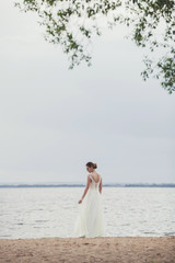 Fototapeta na wymiar charming bride in a wedding dress stands on the shore of the lake