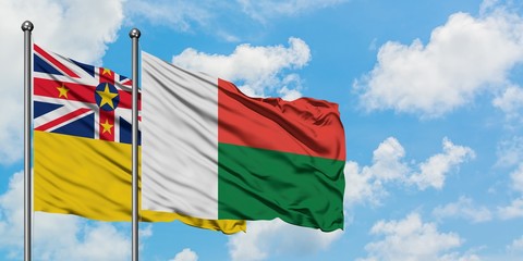 Niue and Madagascar flag waving in the wind against white cloudy blue sky together. Diplomacy...