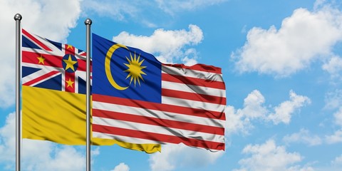 Niue and Malaysia flag waving in the wind against white cloudy blue sky together. Diplomacy concept, international relations.