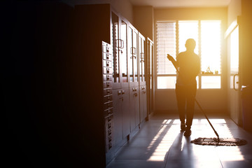 Janitor woman mopping floor in hallway office building or walkway after school or classroom with copy space. Silhouette housekeeper working job with sun light background.