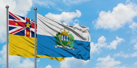 Niue and San Marino flag waving in the wind against white cloudy blue sky together. Diplomacy concept, international relations.