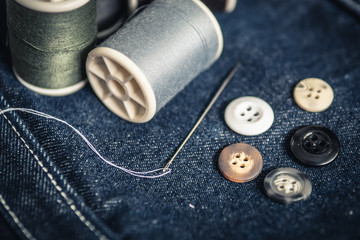 Needle, buttons and spool of thread on jeans fabric