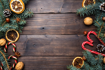 Frame of Christmas tree cones oranges caramel cane nuts on dark wooden background. Copy space. Flat...