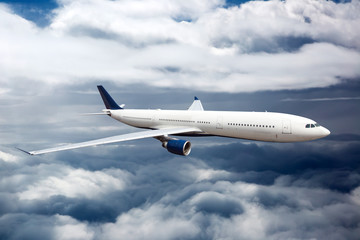 Plakat Side view of white aircraft in flight. The passenger plane flies high between the clouds layers.