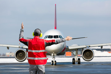 Aviation Marshall / Supervisor meets passenger airplane at the airport. Ground Crew in the signal vest.