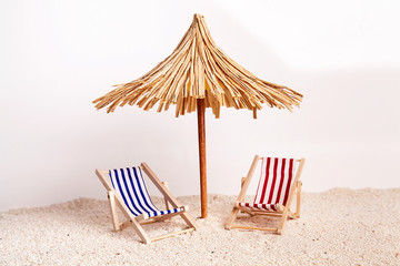 Toy chaise longue and sun umbrella on sandy beach on sunny day at the white background. Relaxation concept.