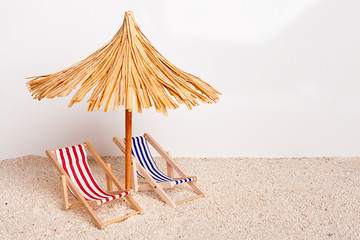Toy chaise longue and sun umbrella on sandy beach on sunny day at the white background. Relaxation...