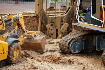 one yellow excavator excavating the ground and one crane bucket picking up mud