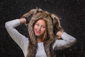 A young beautiful woman in a fur hat with ears, and woolly mittens, smiling provocatively, holding...