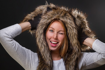A young beautiful woman in a fur hat with ears, and woolly mittens, smiling provocatively,...