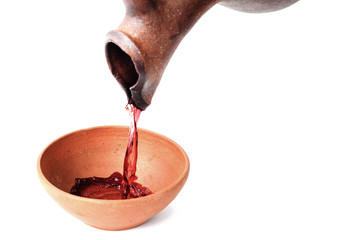 A red wine is pouring from  jug in to the clay cup