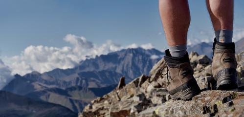 Close up view of high trekking boots and male legs on stony mountain top; dangerous hiking route...