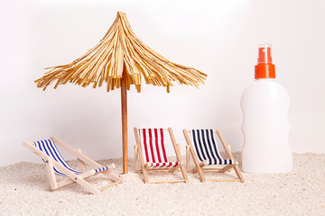 Toy chaise longue and sun umbrella on sandy beach at the white background. Relaxation concept.
