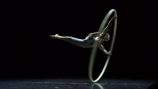 Muscular circus artist in the Cyr Wheel doing difficult tricks slow motion. Concept of concentration and balance