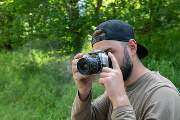 The camera smokes in the hands of photographer takes a photo in nature. young bearded man photographs outdoors.