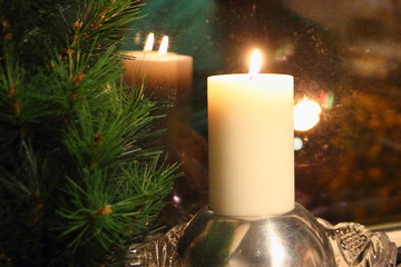 Bright flame of a candle in a shiny ball is reflected in the glass near a fir branch, Christmas holidays