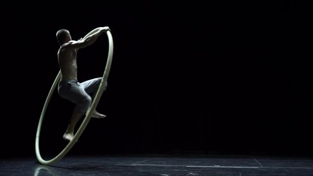 Muscular circus artist in the Cyr Wheel doing difficult tricks slow motion. Concept of concentration and balance