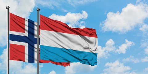 Norway and Luxembourg flag waving in the wind against white cloudy blue sky together. Diplomacy...