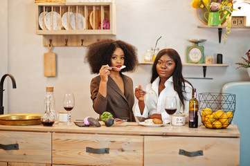 Two african american female friends women spending time at kitchen with wine. Black girlfriends  relaxing at home and eat salad.
