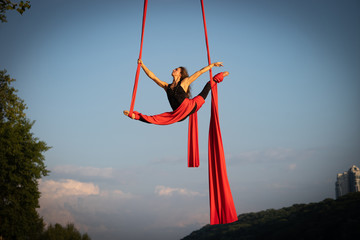 Beautiful and flexible female circus artist dancing with aerial silk on a sky background