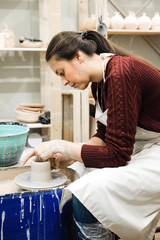 Sculptor woman makes a cup on a potters wheel.