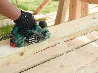 The process of processing a wooden board with a carpenter using an electric planer. Planing boards