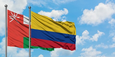 Oman and Colombia flag waving in the wind against white cloudy blue sky together. Diplomacy...