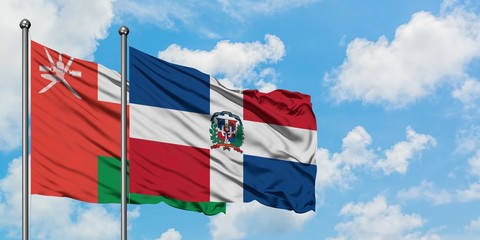 Oman and Dominican Republic flag waving in the wind against white cloudy blue sky together....