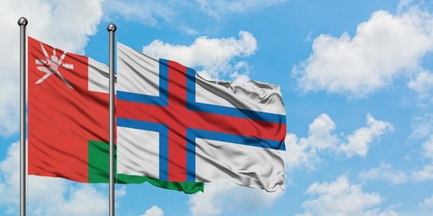 Oman and Faroe Islands flag waving in the wind against white cloudy blue sky together. Diplomacy...