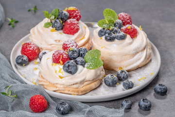 Mini pavlova meringue cakes with fresh raspberries and blueberries with mint leaves.