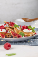 Pancakes with raspberries, figs, yogurt, coconut zest, honey and mint leaves on a plate.