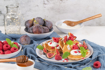 Pancakes with raspberries, figs, yogurt, coconut zest, honey and mint leaves on a plate.