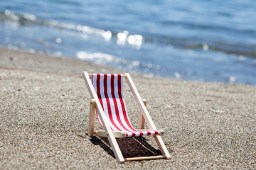 Toy chaise longue on sandy beach on sunny day at the blue sea background. Relaxation concept.