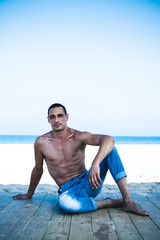 Fototapeta na wymiar young muscular man in denim pants resting and posing on the beach