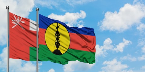 Oman and New Caledonia flag waving in the wind against white cloudy blue sky together. Diplomacy...