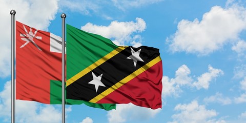 Oman and Saint Kitts And Nevis flag waving in the wind against white cloudy blue sky together....