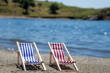 Toy chaise longue on sandy beach on sunny day at the blue sea background. Relaxation concept.