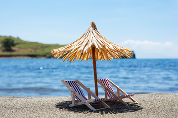 Toy chaise longue and sun umbrella on sandy beach on sunny day at the blue sea background....