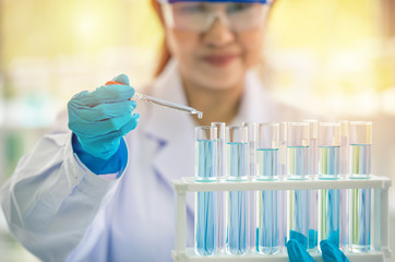 asia women scientist shows glass tube with blue liquid inside in the laboratory