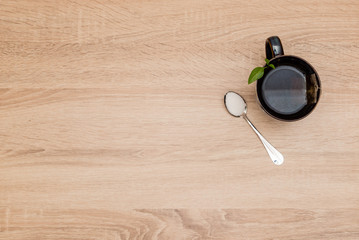 A mug with tea and a spoon with suger on a wooden table