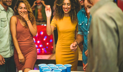 Group of happy friends playing beer pong in hostel bar - Young trendy people having fun doing party...