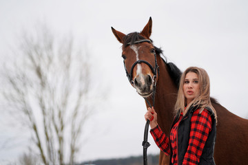 Obraz premium A beautiful girl in a fashionable shirt walks with horse in early winter. space for text on white background