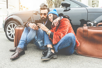 Fashion couple checking map on smartphone app - Trendy people having fun traveling with convertible car - Travel, relationship and technology trends concept - Focus on faces - obrazy, fototapety, plakaty
