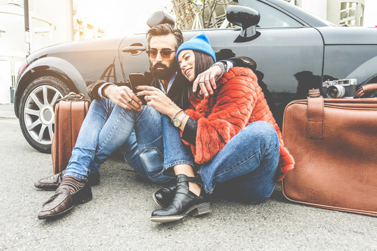 Fashion couple checking map on smartphone app - Trendy people having fun traveling with convertible car - Travel, relationship and technology trends concept - Focus on faces - Powered by Adobe