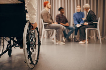 Close-up of disabled man sitting on wheelchair with group of people talking to each other in the background