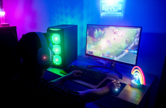 Young gamer playing online with neon lights in background - Male guy having fun gaming and streaming in internet with pc - Technology millennial trends, entertainment concept - Focus on right hand