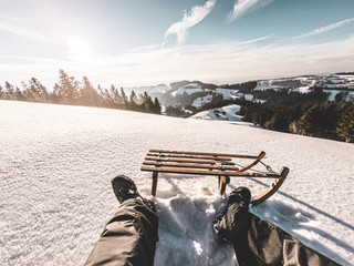 Pov view of young man looking the sunset on snow high mountains with vintage sledding - Legs view...