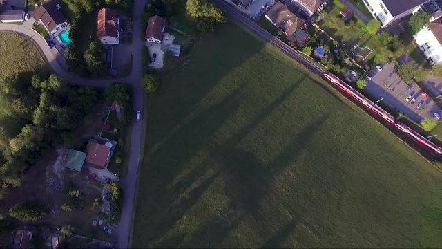 Aerial view of a red train and a car entering a village. SBB CFF FFS
